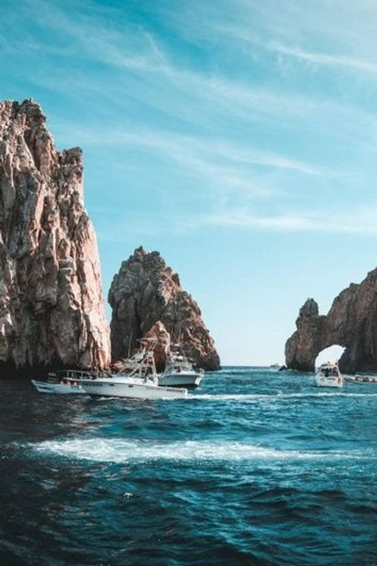 This may contain: two boats are in the water near some large rocks and an arch shaped rock formation