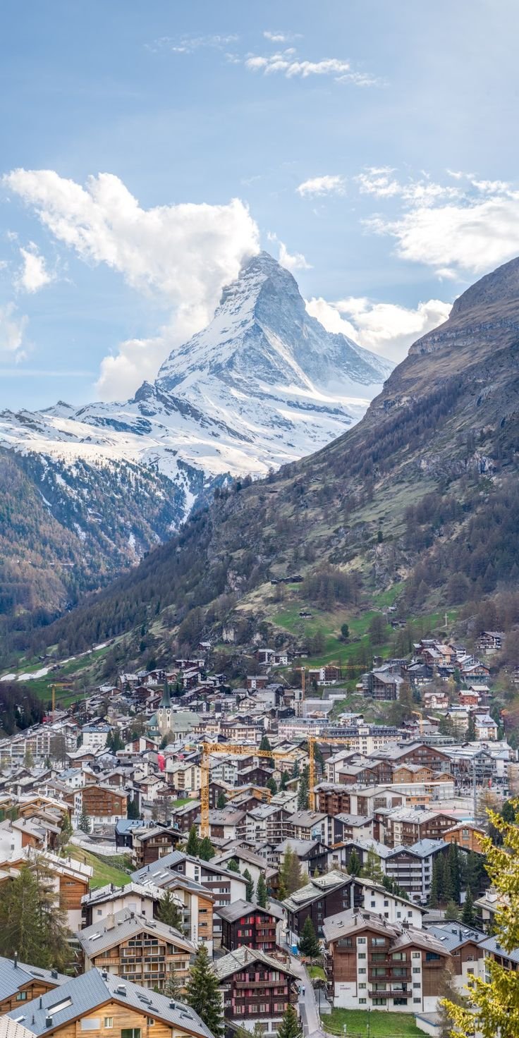 This may contain: a city with mountains in the background and snow on the top of the mountain behind it