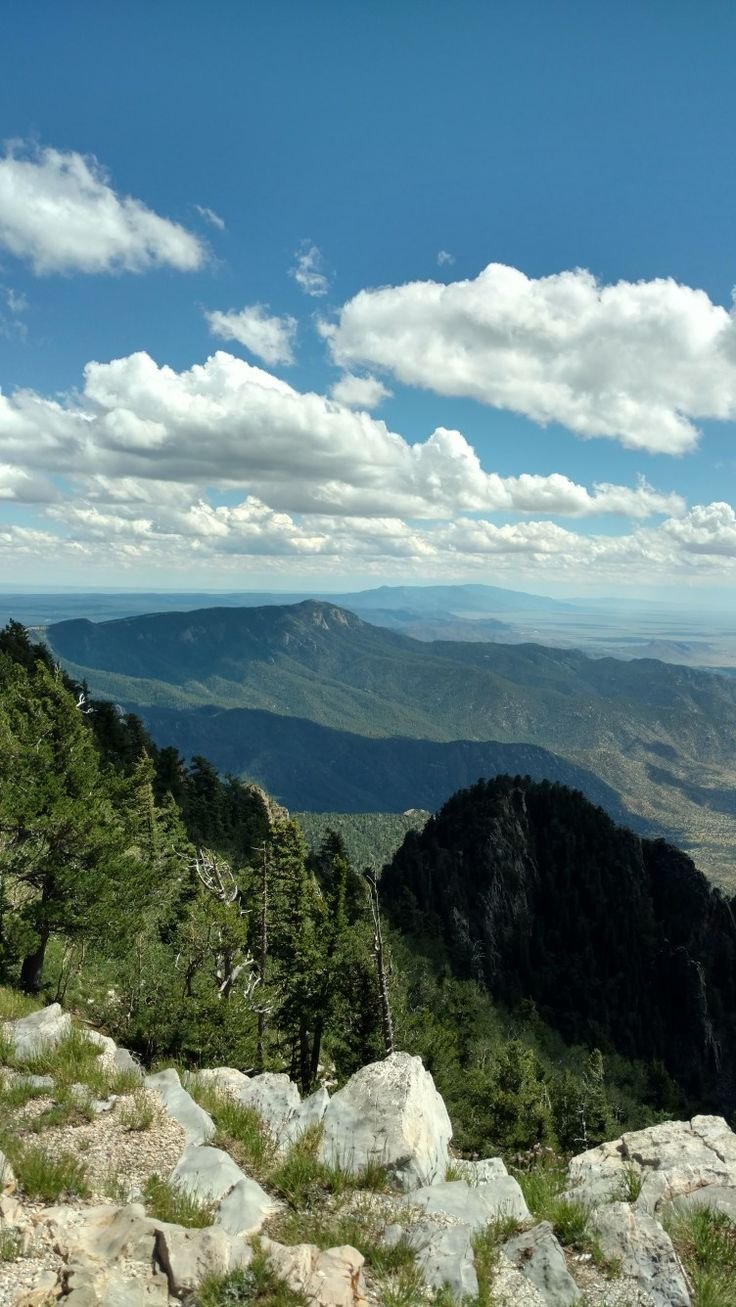 This may contain: a view from the top of a mountain looking down at some trees and mountains in the distance