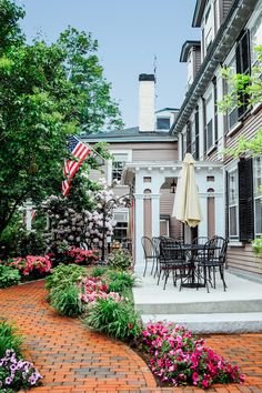 This may contain: an outdoor patio with flowers and tables in the foreground, surrounded by brick pavers