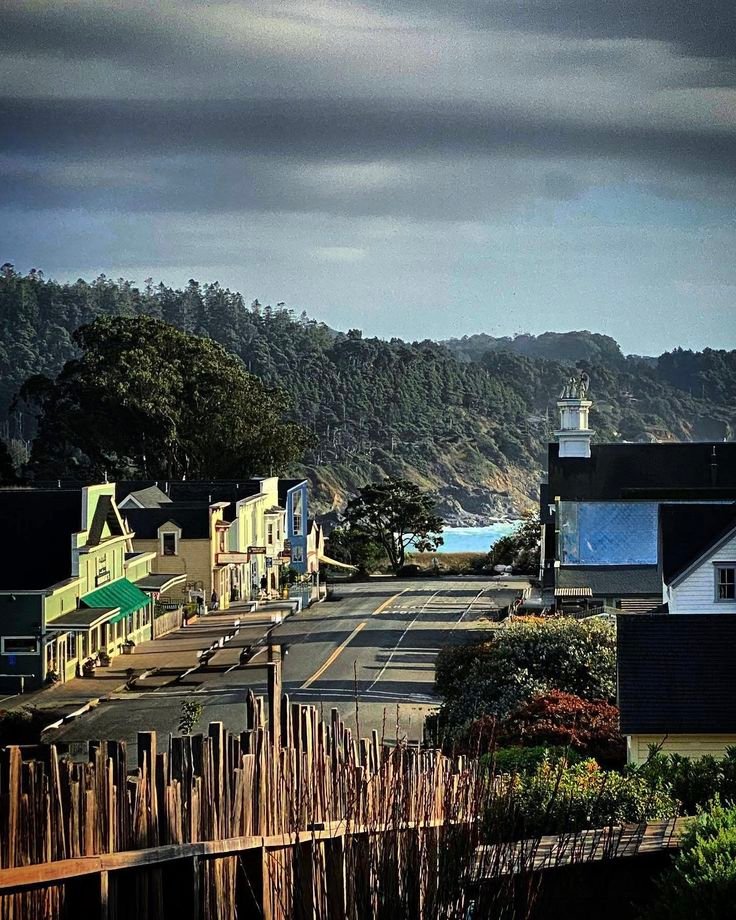 This may contain: an empty street with houses and mountains in the background
