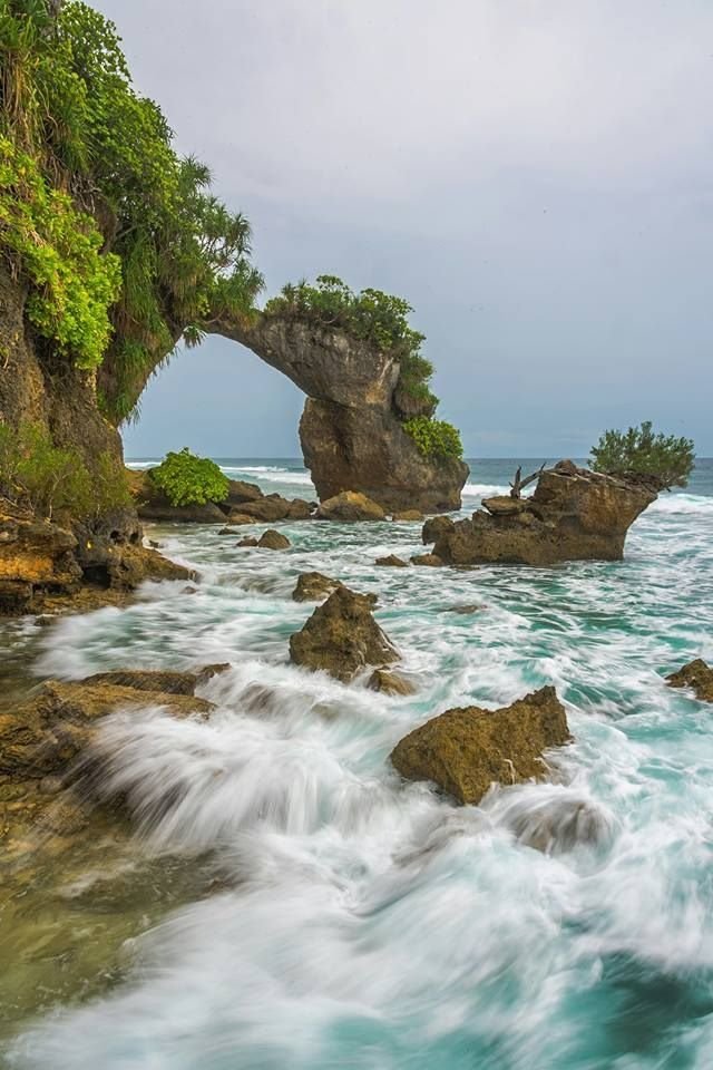 This may contain: the ocean with rocks and trees on it is very blue, green and white in color