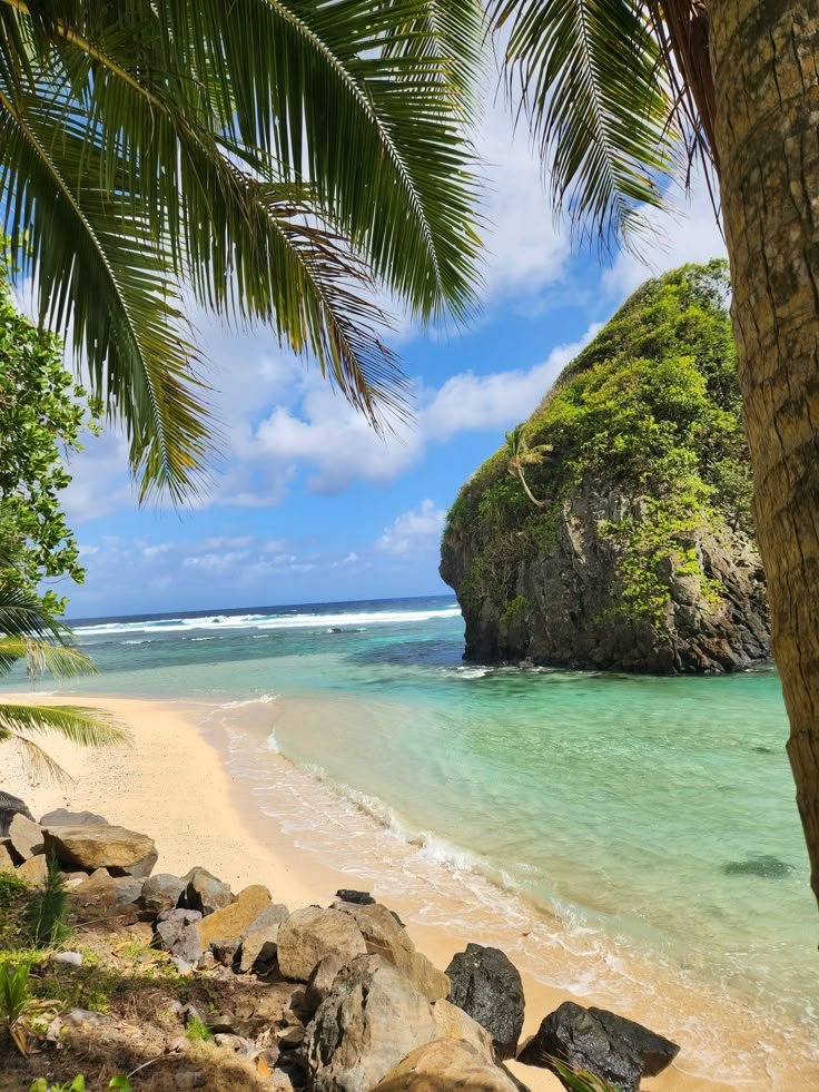 This may contain: the beach is surrounded by palm trees and rocks