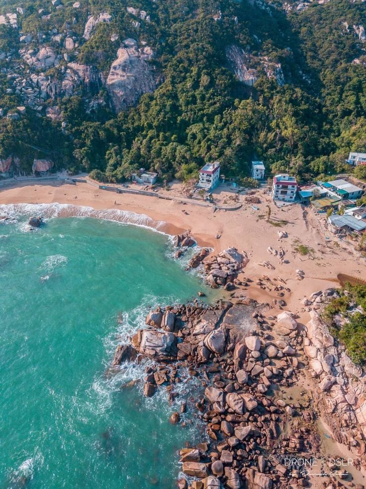 This may contain: an aerial view of a beach and the ocean with houses on it, surrounded by trees