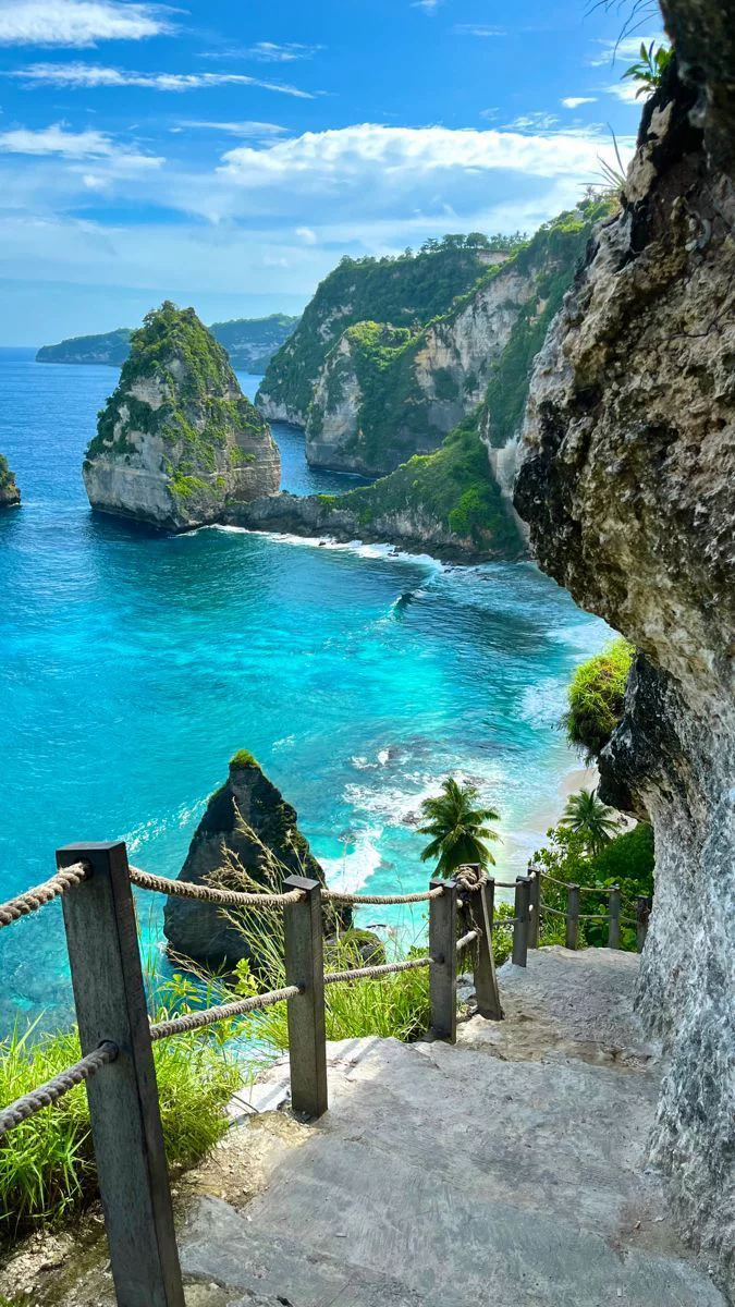 This may contain: stairs lead down to the blue water and sandy beach with cliffs in the background,