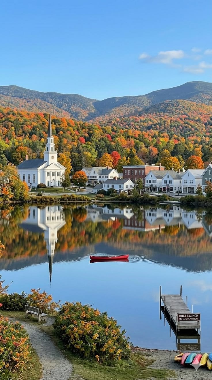 This may contain: a lake surrounded by mountains and houses in the fall
