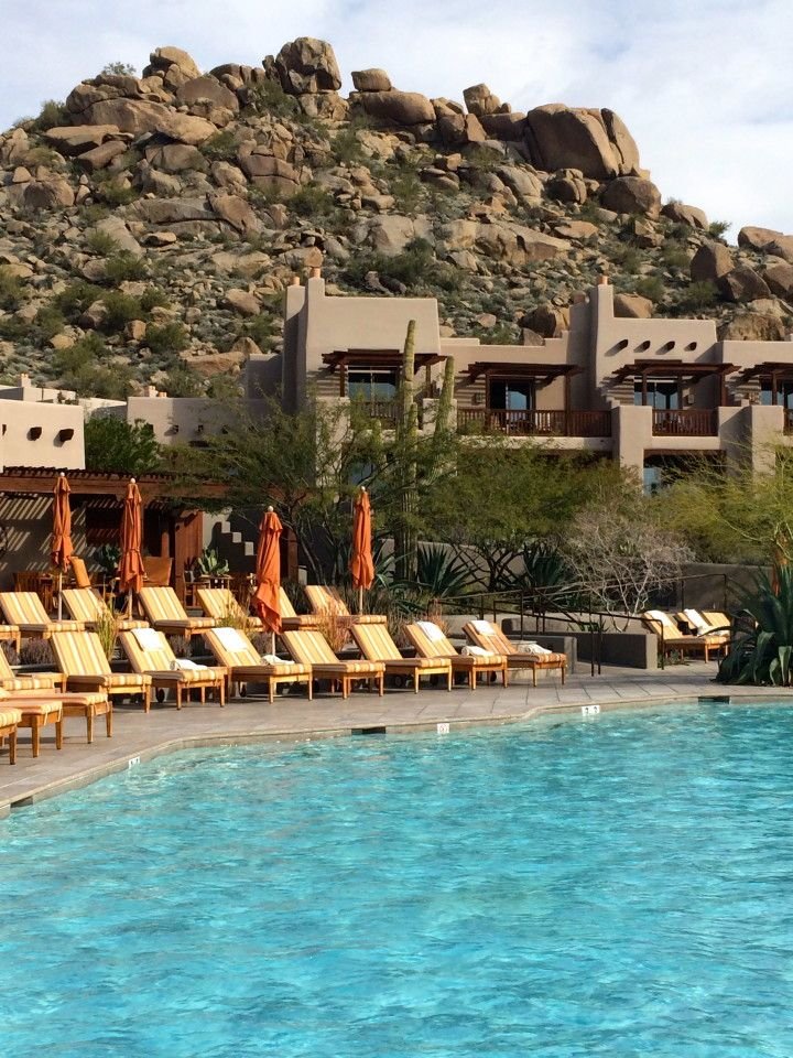 This may contain: an outdoor swimming pool with lounge chairs and mountains in the background