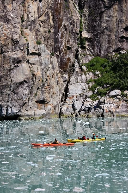 This may contain: two people in kayaks paddling on the water next to large rocks and cliffs