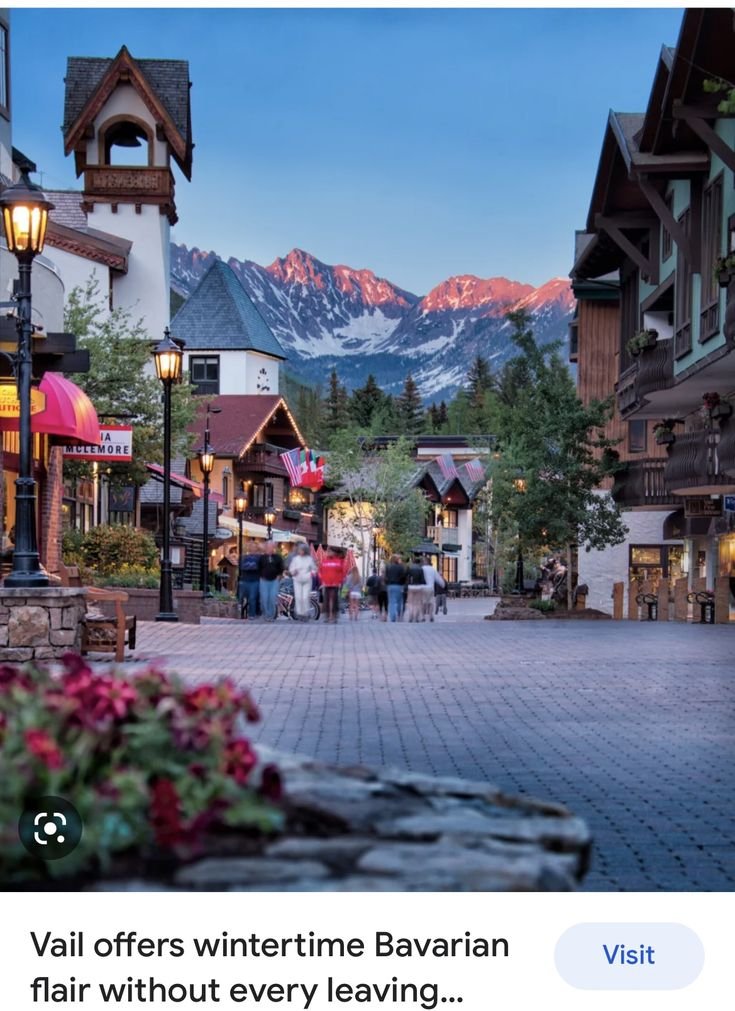 This may contain: people are walking down the street in front of some buildings with mountains in the background
