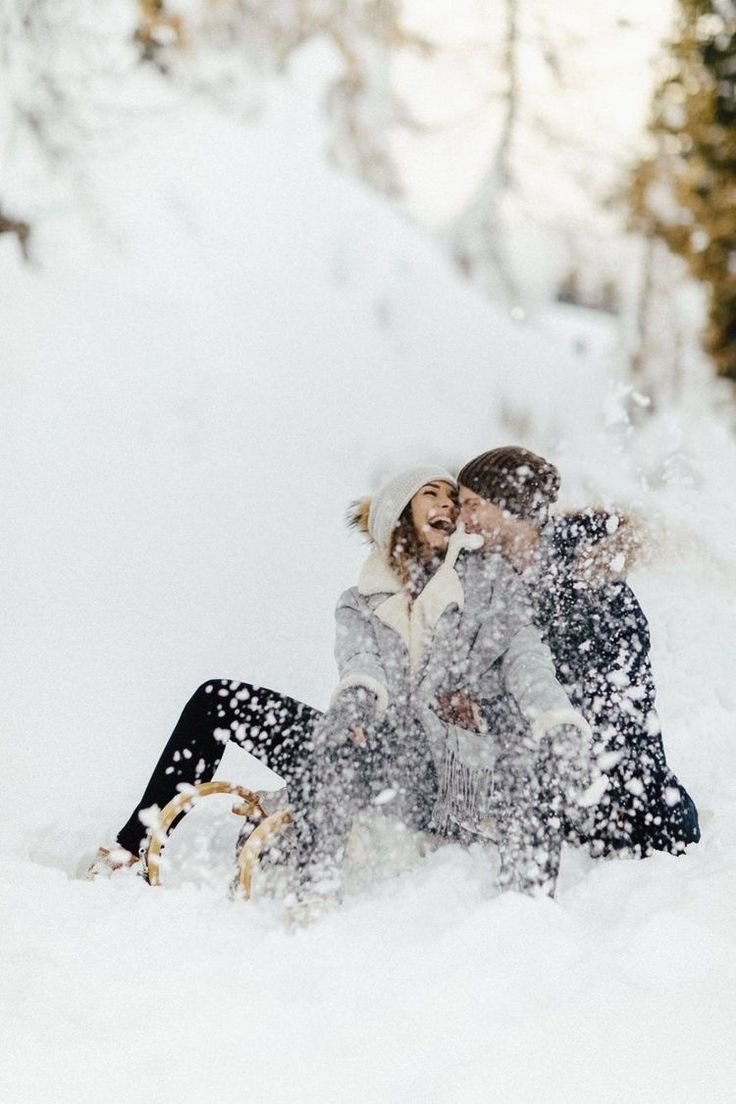 This may contain: two people are sitting in the snow and laughing