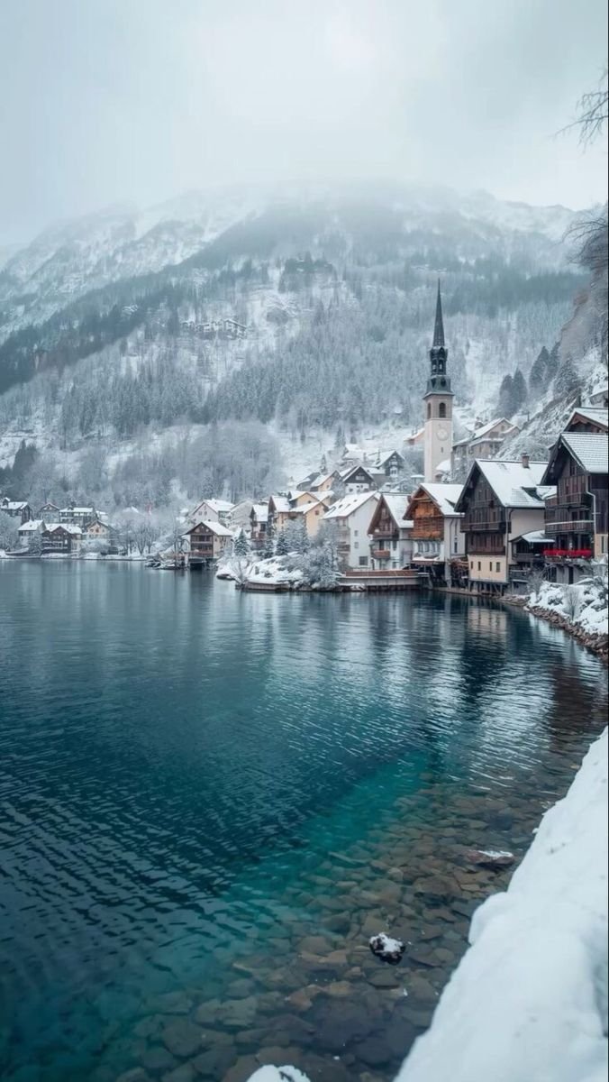 This may contain: a lake surrounded by snow covered mountains in the middle of winter with buildings on both sides