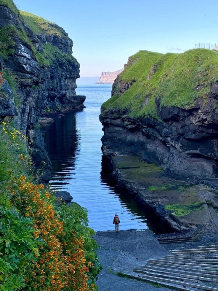 This may contain: a person standing on the edge of a cliff next to some water and cliffs with green grass