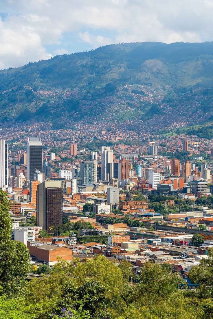 This may contain: a city with mountains in the background and trees on the foreground, surrounded by greenery