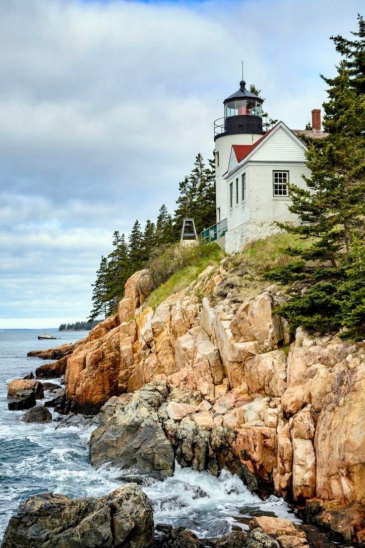 This may contain: a light house on top of a rocky cliff next to the ocean with trees around it