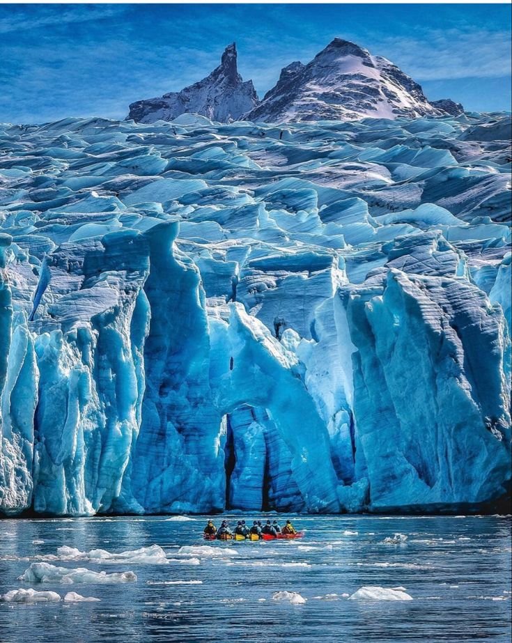 This may contain: a group of people paddling in a boat near an iceberg