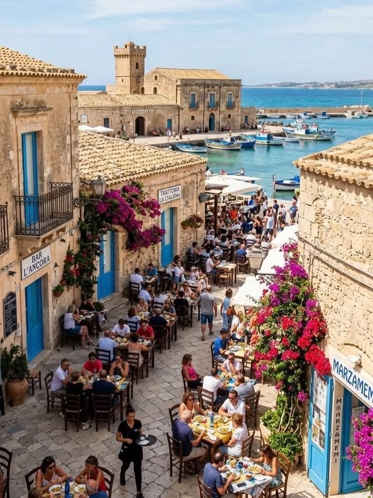 This may contain: people are sitting at tables in an old town by the water
