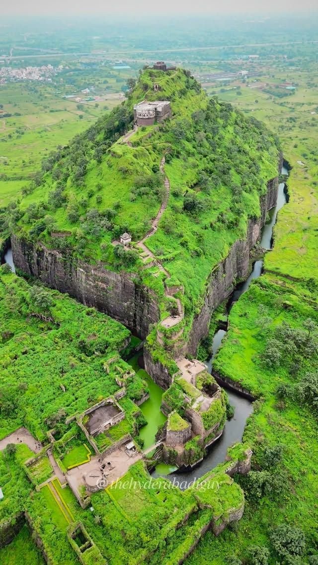 This may contain: an aerial view of the green countryside and river in front of a large rock formation