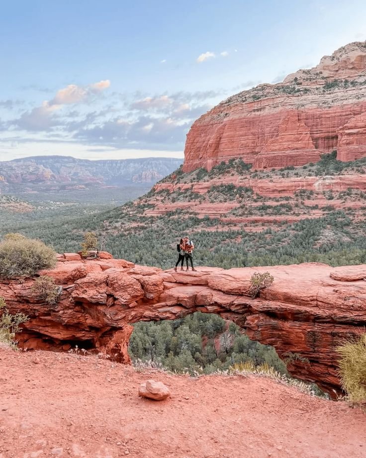 This may contain: a man standing on top of a red rock cliff