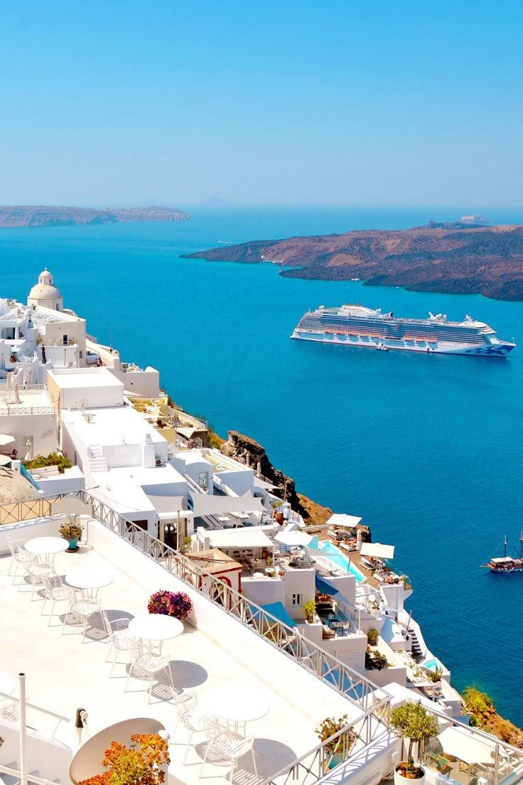 This may contain: a cruise ship is in the water next to some white buildings and tables with umbrellas