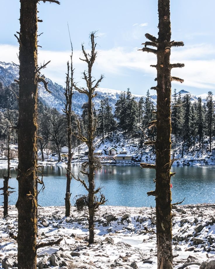 This may contain: snow covers the ground and trees in front of a lake