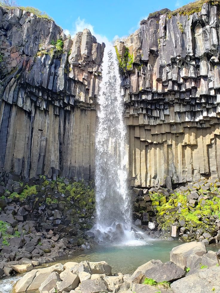 This may contain: a large waterfall cascading over rocks into a river next to a cliff face