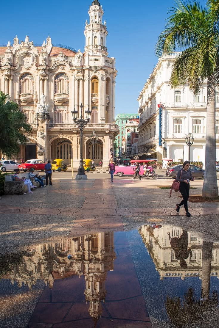 This may contain: people walking on the street in front of an old building with a clock tower and palm trees