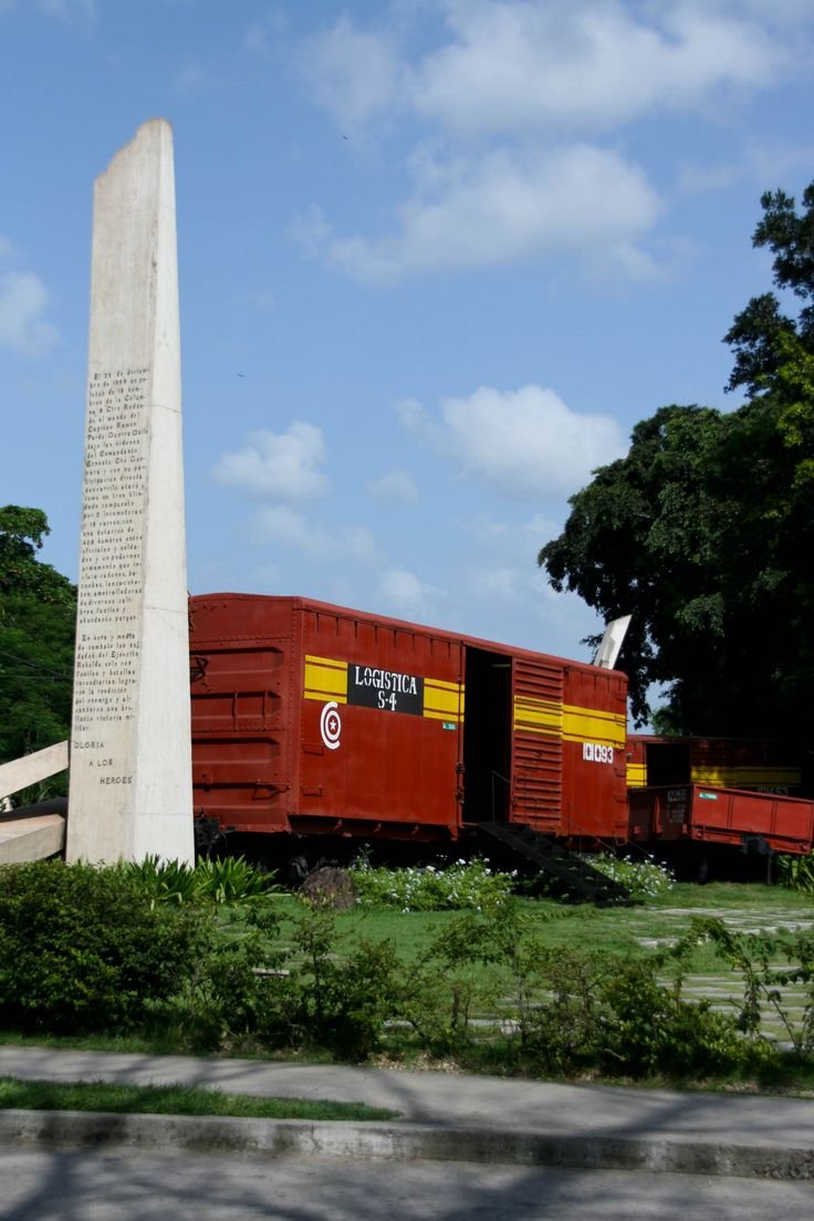 This may contain: a red train traveling past a tall white obelisk