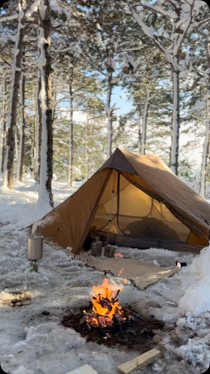 This may contain: a tent sitting in the snow next to a campfire