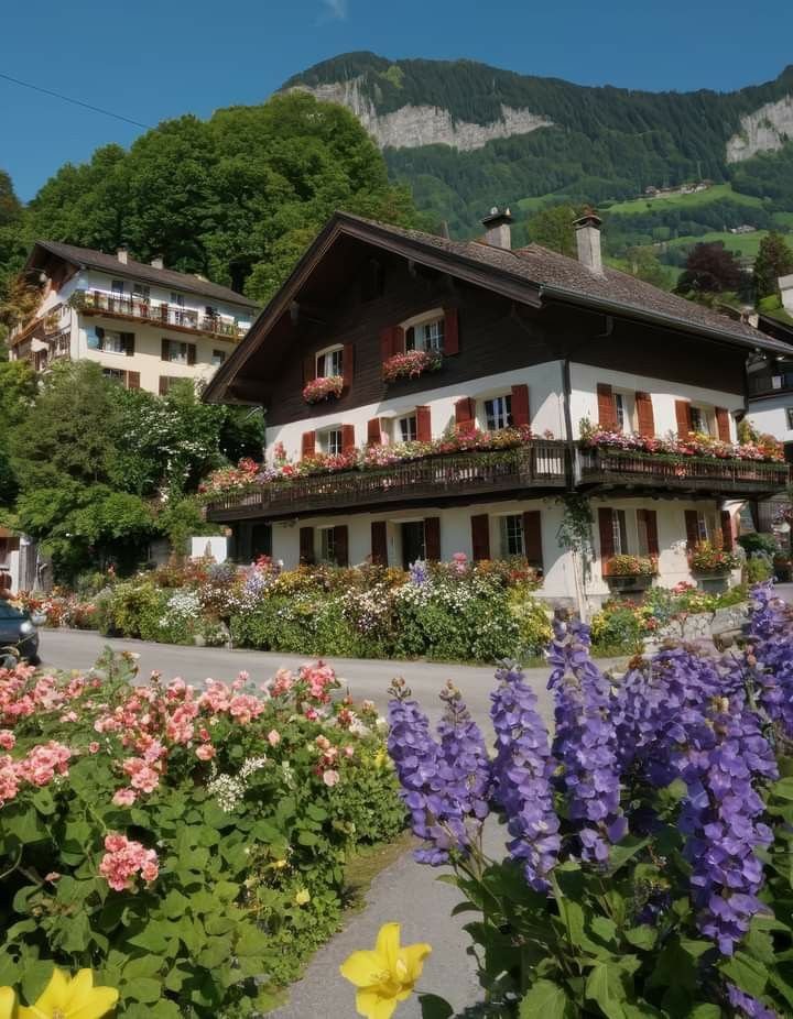 This may contain: a house with flowers in front of it and mountains in the backgrouds