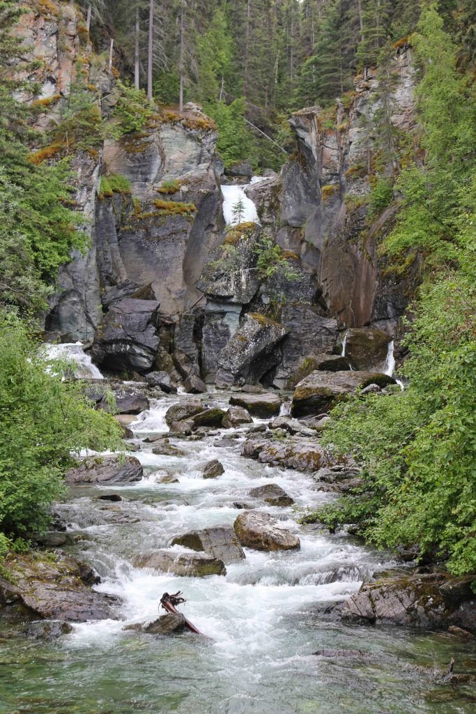 This may contain: a man is wading in the water near some rocks and trees with a waterfall behind him