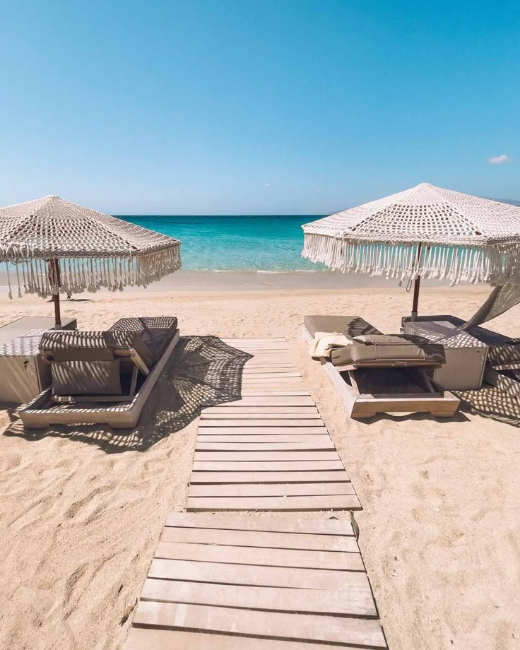 This may contain: lounge chairs and umbrellas on the beach with clear blue water in the back ground