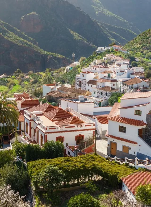 This may contain: an aerial view of some white houses and mountains in the distance with trees on either side