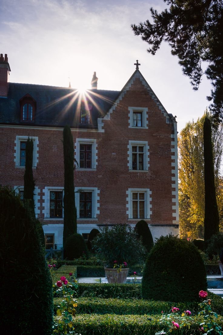 This may contain: the sun shines brightly in front of a large brick building with hedges and flowers