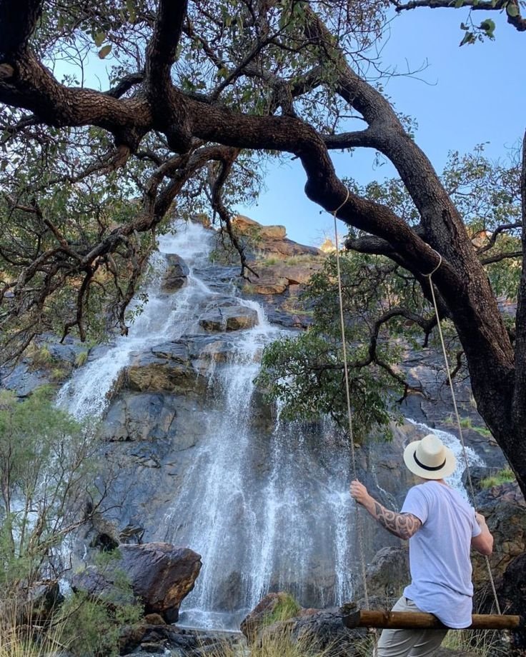 This may contain: a man standing next to a waterfall with a rope hanging from it's side