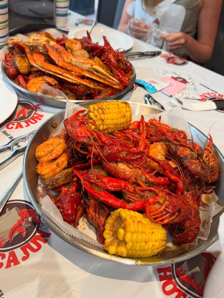This may contain: two plates filled with cooked craws and corn on the cob at a restaurant
