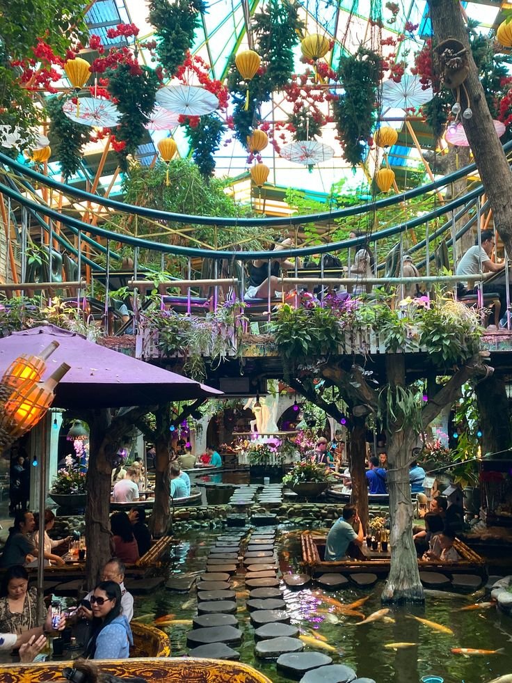 This may contain: people sitting at tables in a garden with lots of plants and flowers hanging from the ceiling