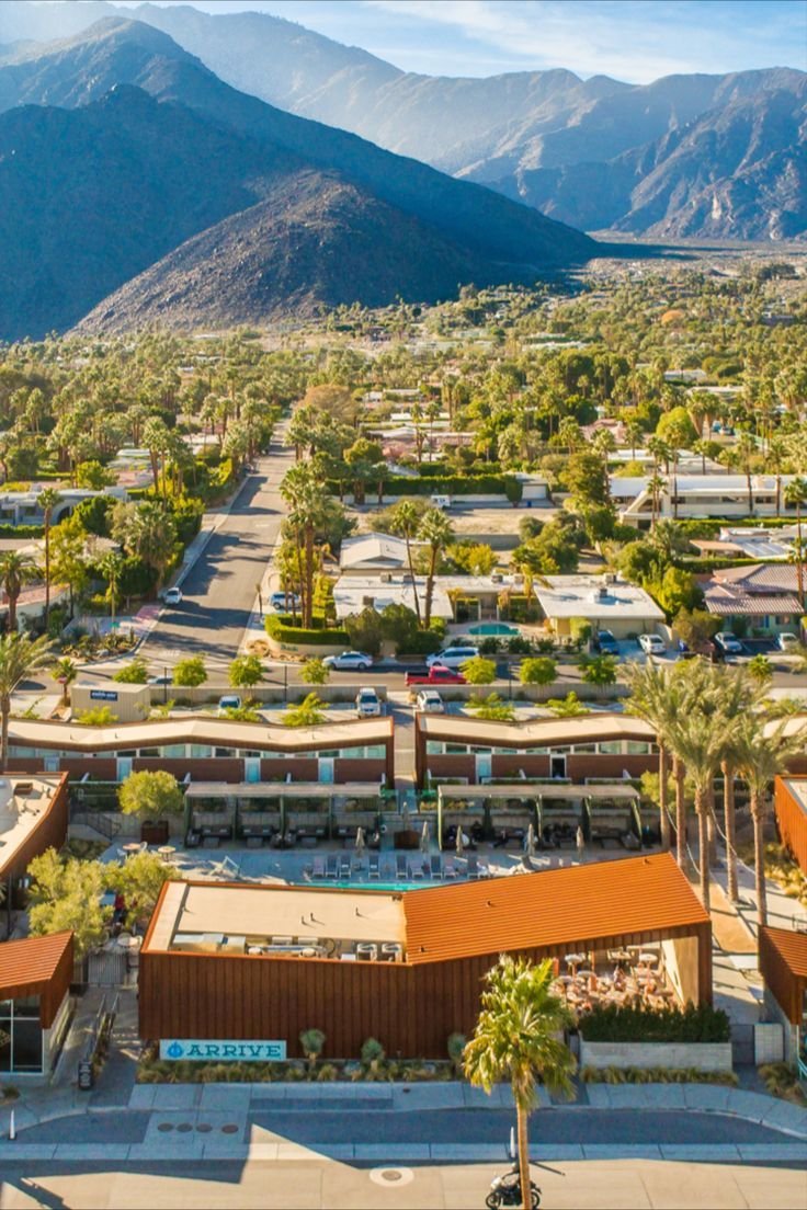 This may contain: an aerial view of a town with mountains in the background and palm trees surrounding it