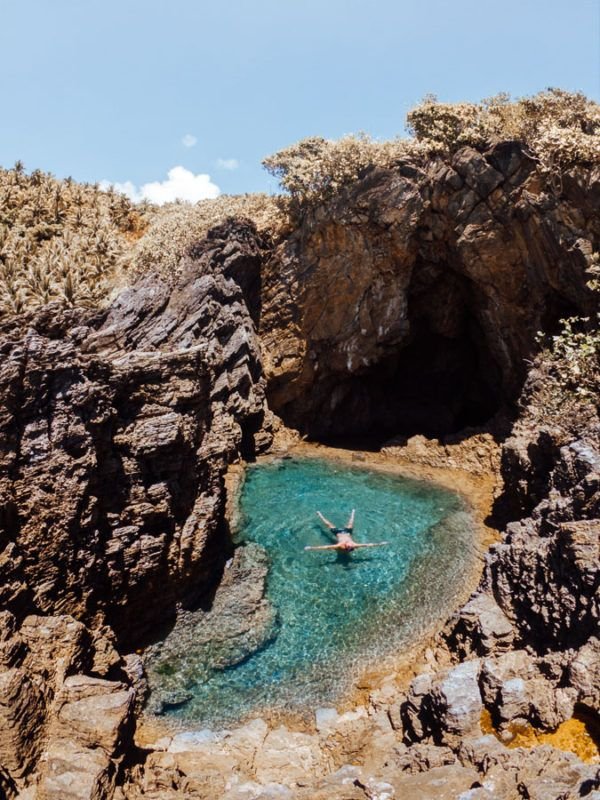 This may contain: a person is swimming in the blue water near some rocks and cliffs on a sunny day