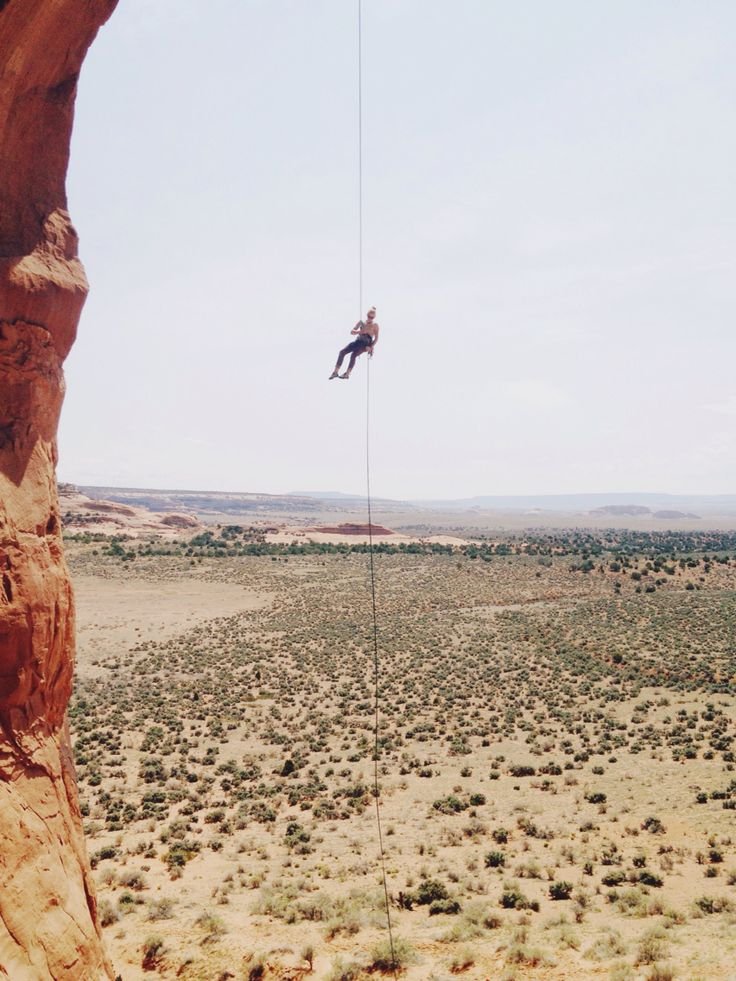 This may contain: a man on a rope high in the air above a desert landscape with rocks and bushes