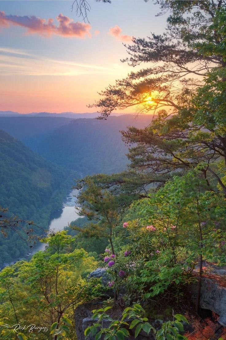 This may contain: the sun is setting on top of a mountain overlooking a valley and river in the distance