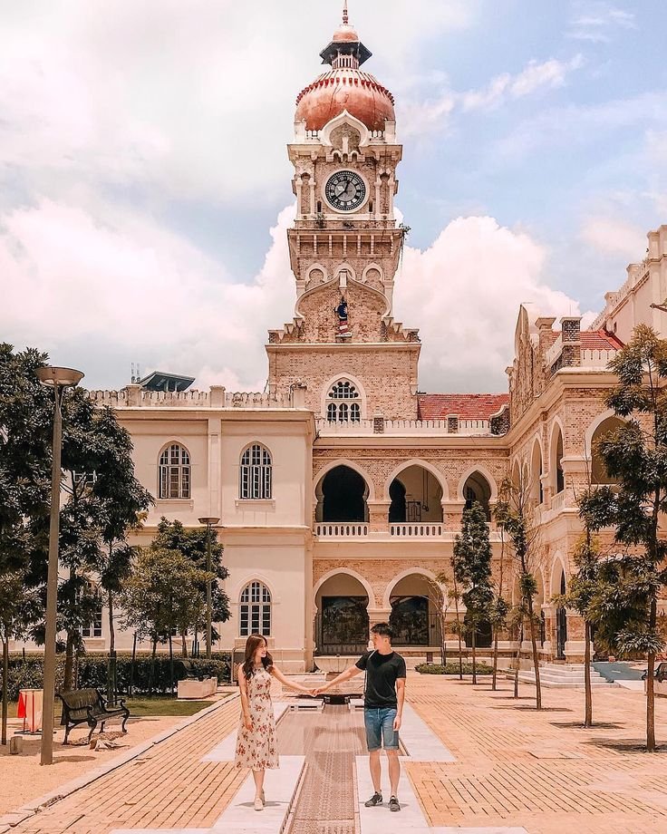 This may contain: two people standing in front of a large building with a clock tower on the top