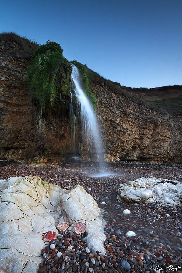 This may contain: there is a waterfall in the background with rocks on the ground and water coming from it