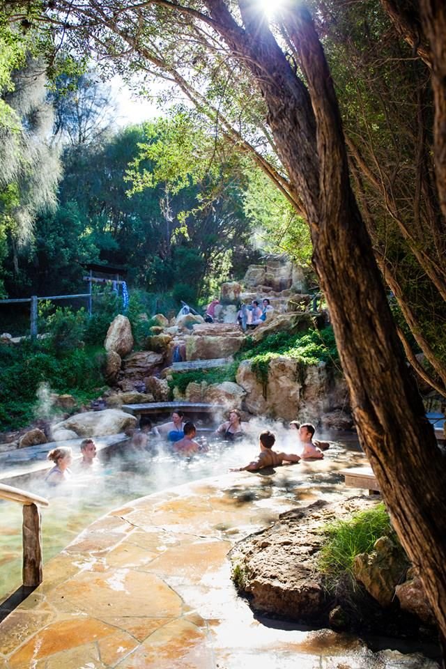 This may contain: several people are in the water at a hot springs area with rocks and trees around them