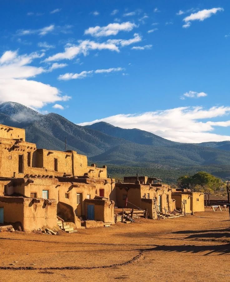 This may contain: an adobe village in the desert with mountains in the backgrouds and clouds in the sky