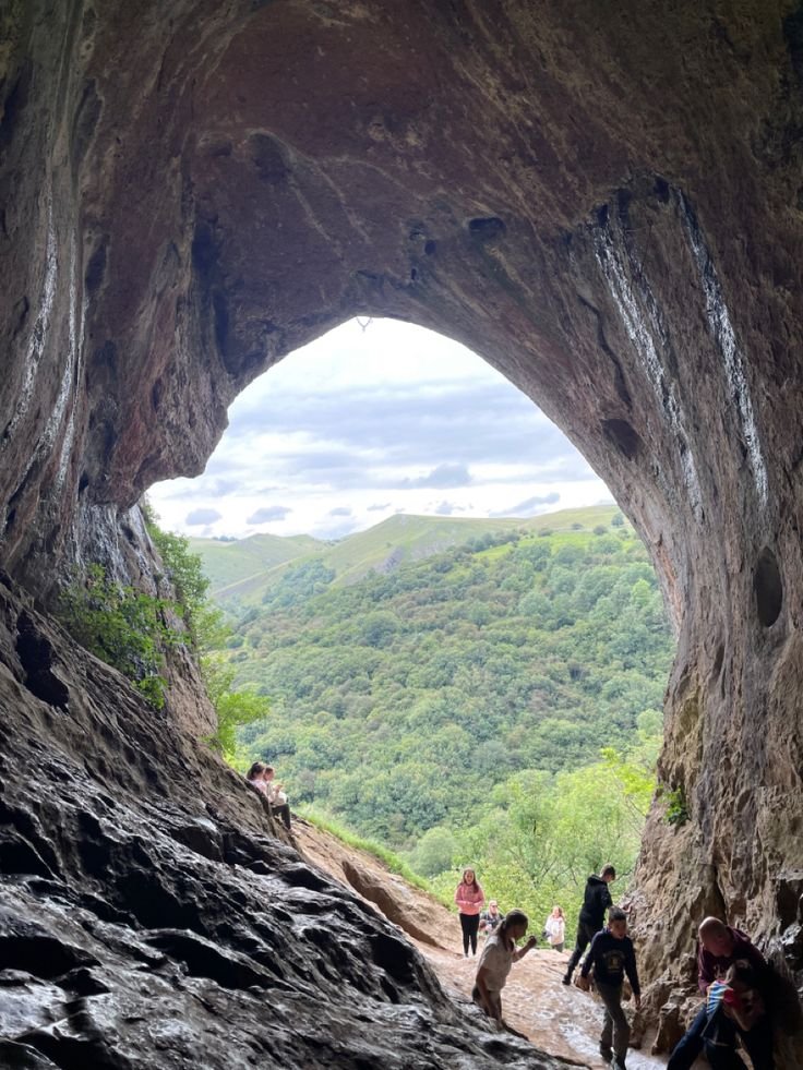 This may contain: the view from inside a cave looking down at trees and mountains in the distance with sunlight coming through