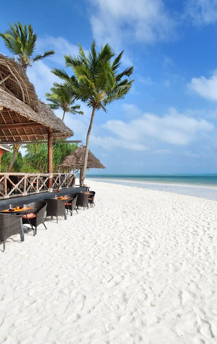 This may contain: an empty beach with chairs and umbrellas on the sand next to the ocean in front of palm trees