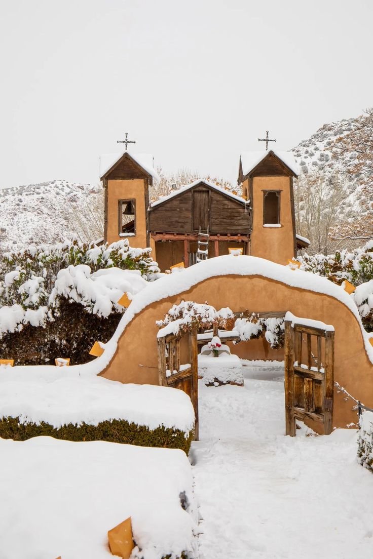 This may contain: an arch covered in snow next to two wooden buildings