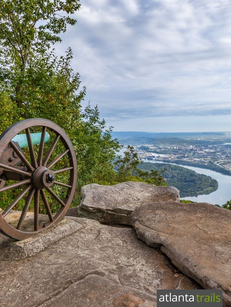 This may contain: an old wagon wheel on top of a rock overlooking a river and town in the distance