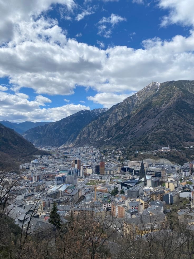 This may contain: a city with mountains in the background under a blue sky filled with white fluffy clouds