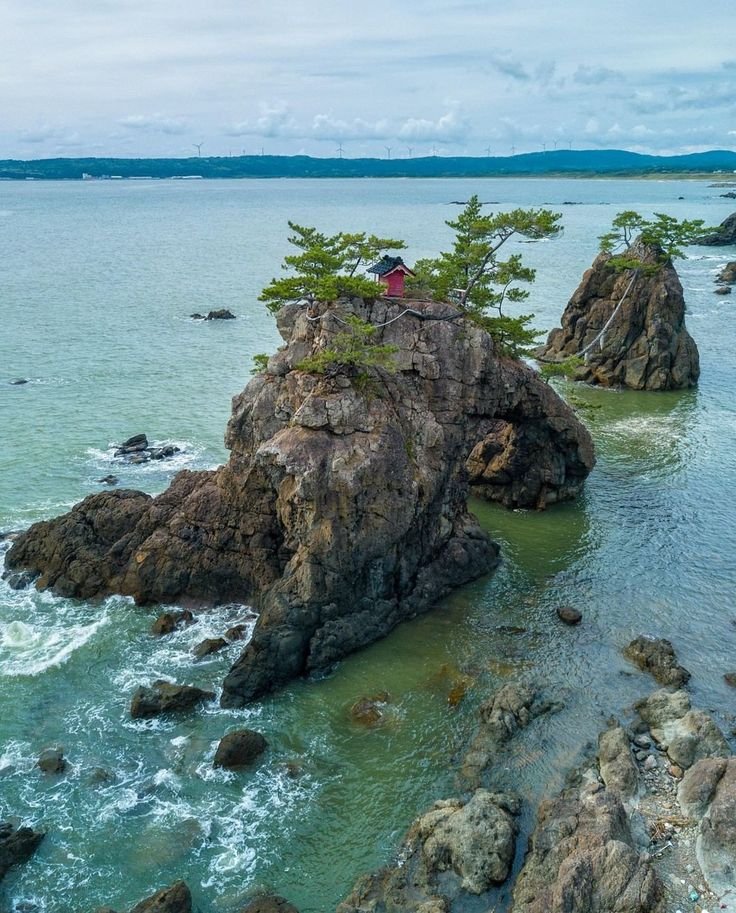 This may contain: a person standing on top of a rock in the ocean near some rocks and water